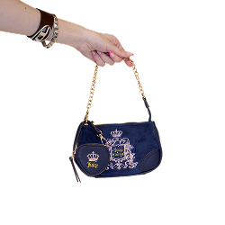A hand holds a navy Juicy Couture handbag with gold chain and crest, featuring a heart-shaped charm.