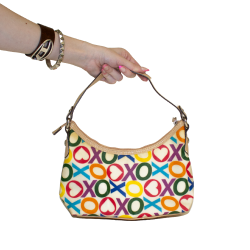 A hand holds a colorful handbag with a bold XO pattern (XOXO band), featuring hearts and circles.