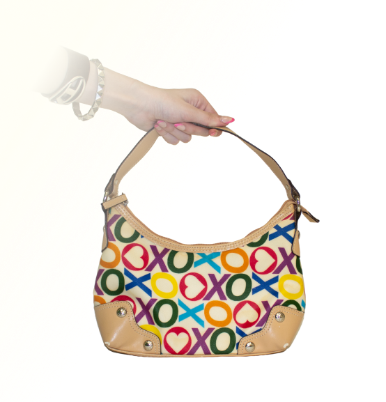 A hand holds a colorful handbag to show back view of Harley with a bold XO pattern (XOXO band), featuring hearts and circles.