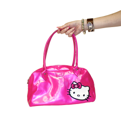 A hand holds a shiny hot pink Hello Kitty handbag with a bow, showcasing a playful and stylish accessory.