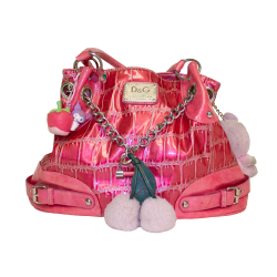 A shiny pink handbag with chain straps, pom-pom accents, and an alligator textured pattern, featuring a prominent D&G logo on the front.