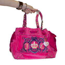 A large hot pink juicy couture purse with bedazzled keychains and blue/gold embroidery on the front, featuring a crown and the letters J and C.
