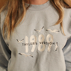 Model wearing light blue sweatshirt that reads 1989 Taylor's Version surrounded by seagulls.