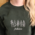 Model wearing dark green sweatshirt that reads Folklore.