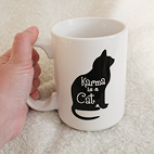 Front view of a white mug with a black cat that reads Karma is a Cat.