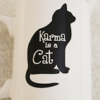 Close-up view of a white mug with a black cat that reads Karma is a Cat.