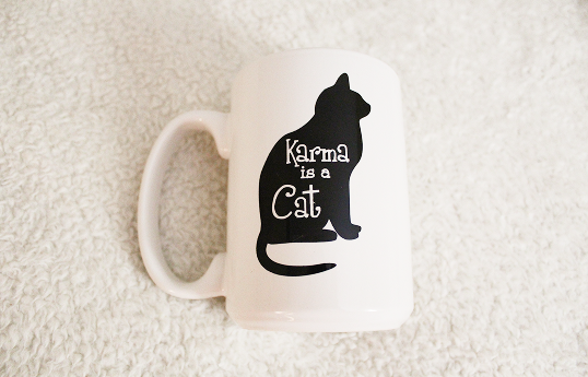 A white mug with a black cat that reads Karma is a Cat.