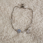 Overshot view of a silver bracelet that features a white crescent moon and a blue saturn planet.