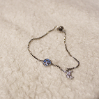 Overshot view of a silver bracelet that features a white crescent moon and a blue saturn planet.