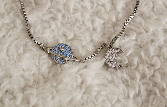 A silver bracelet that features a white crescent moon and a blue saturn planet.