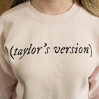 Model wearing a light pink sweathirt that reads (Taylor's Version).