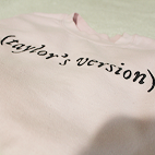 Angled view of a light pink sweathirt that reads (Taylor's Version).